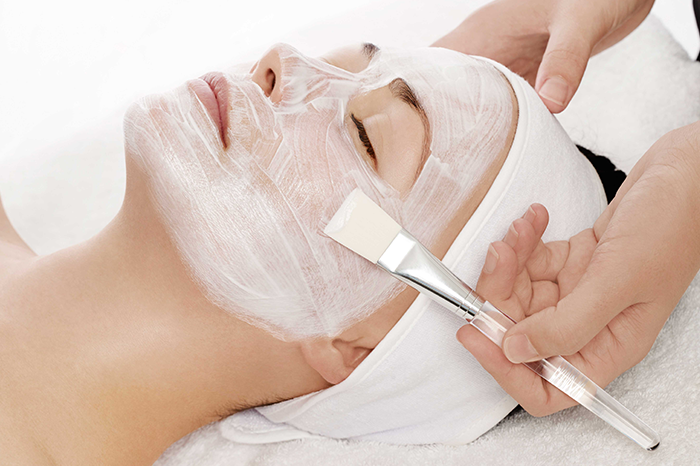 Woman receiving facial with a white mask and brush
