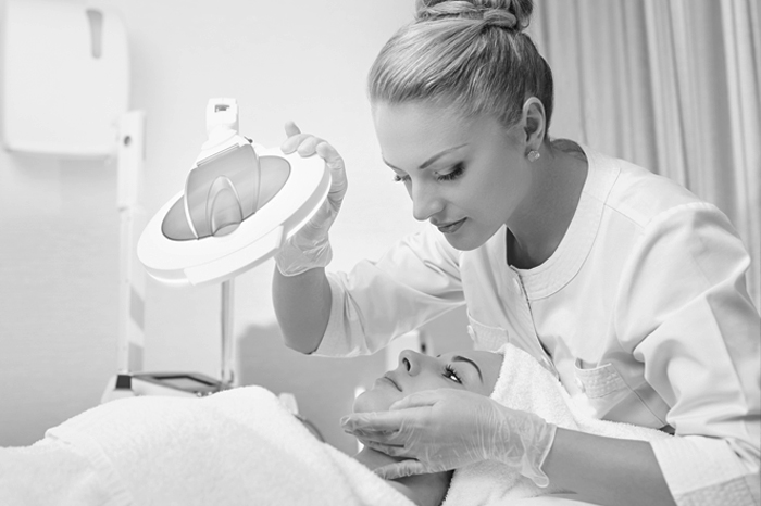 Black and white, woman holding a light on another woman's face during facial