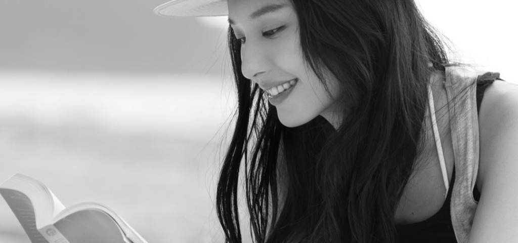 Black and white image of woman in a sun hat reading a book