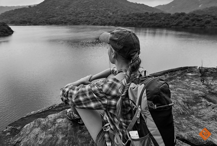 Black and white image of woman sitting on a rock, staring at the lake and mountains