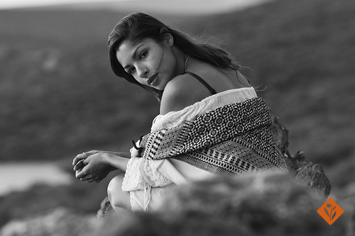 Black and white, woman in a white dress, sitting on a rock, looking over her shoulder