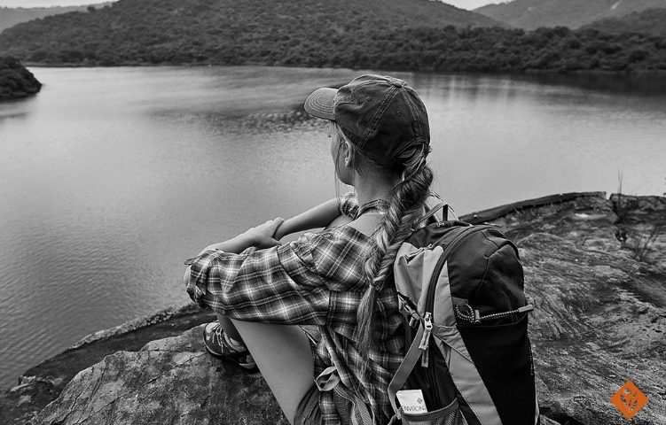 Black and white, woman sitting on a rock, looking at the lake and mountains